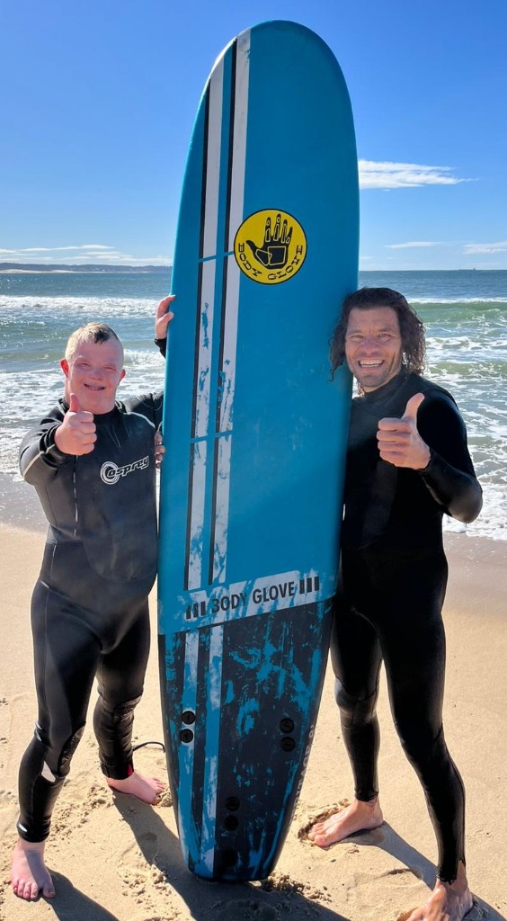 Child standing with surfboard thumbs up on the beach